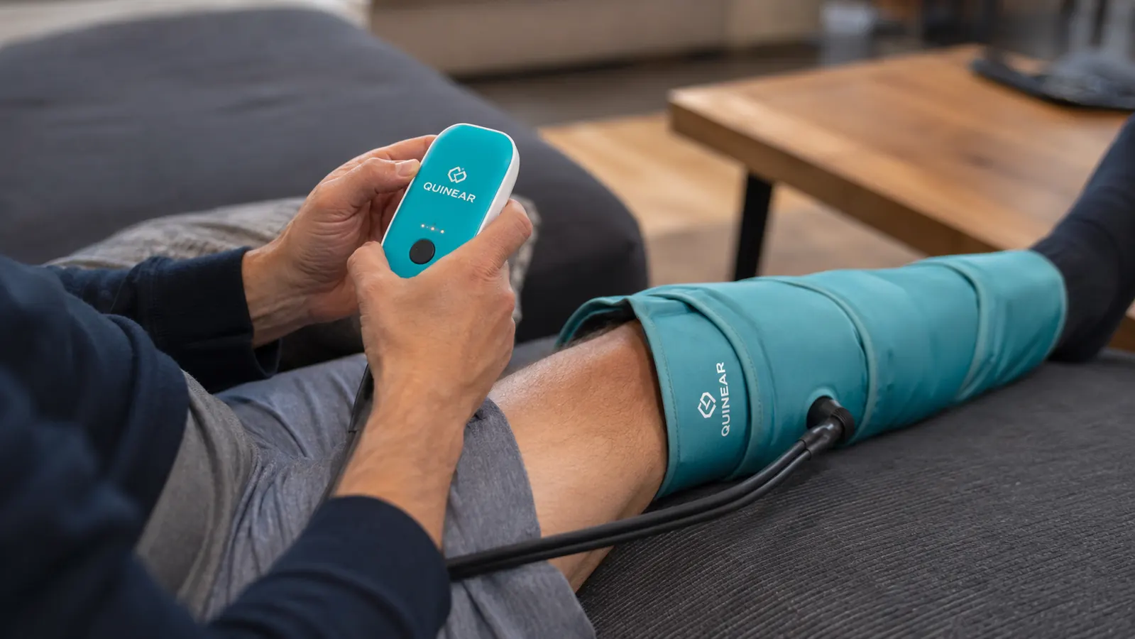Close-up of a hand holding the QUINEAR control unit while the compression boot inflates around a calf