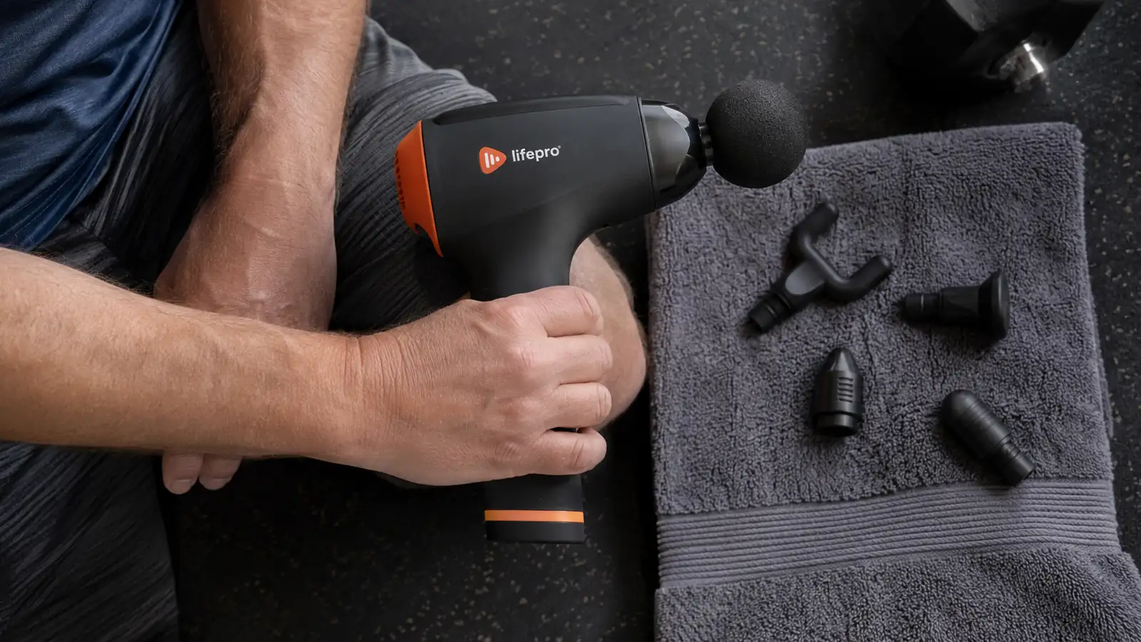 Close-up of a hand holding the Lifepro massage gun with attachment heads laid out beside it