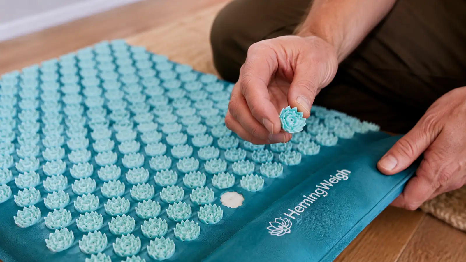 Close-up of a hand inspecting one loose plastic spike disc that has popped off the HemingWeigh mat