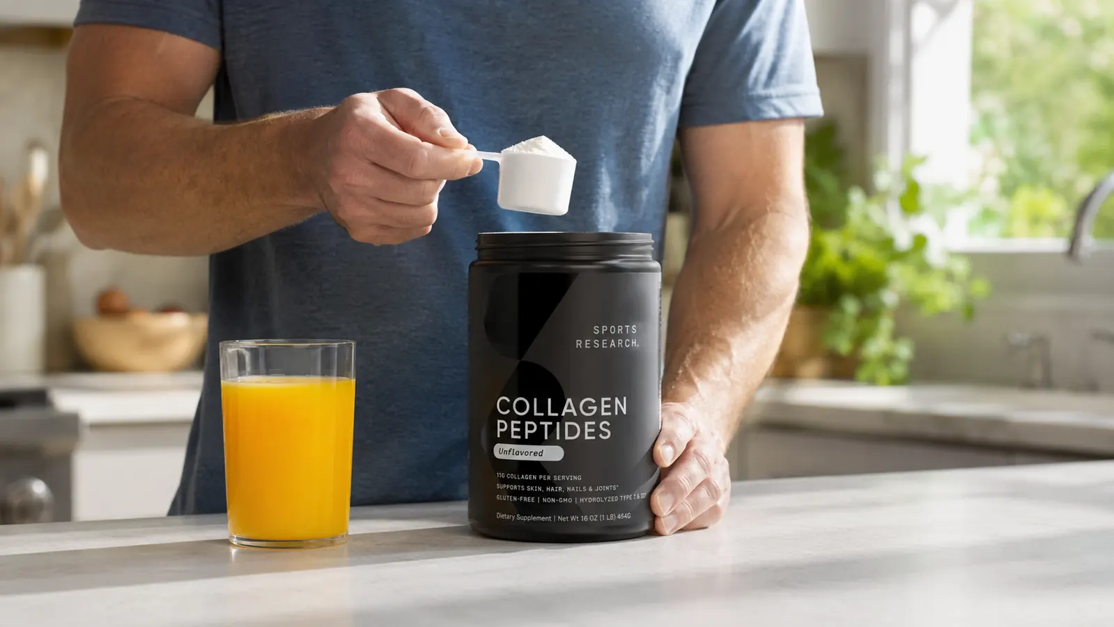 Hand holding a scoop of Sports Research Collagen Peptides powder over an open tub next to a glass of orange juice