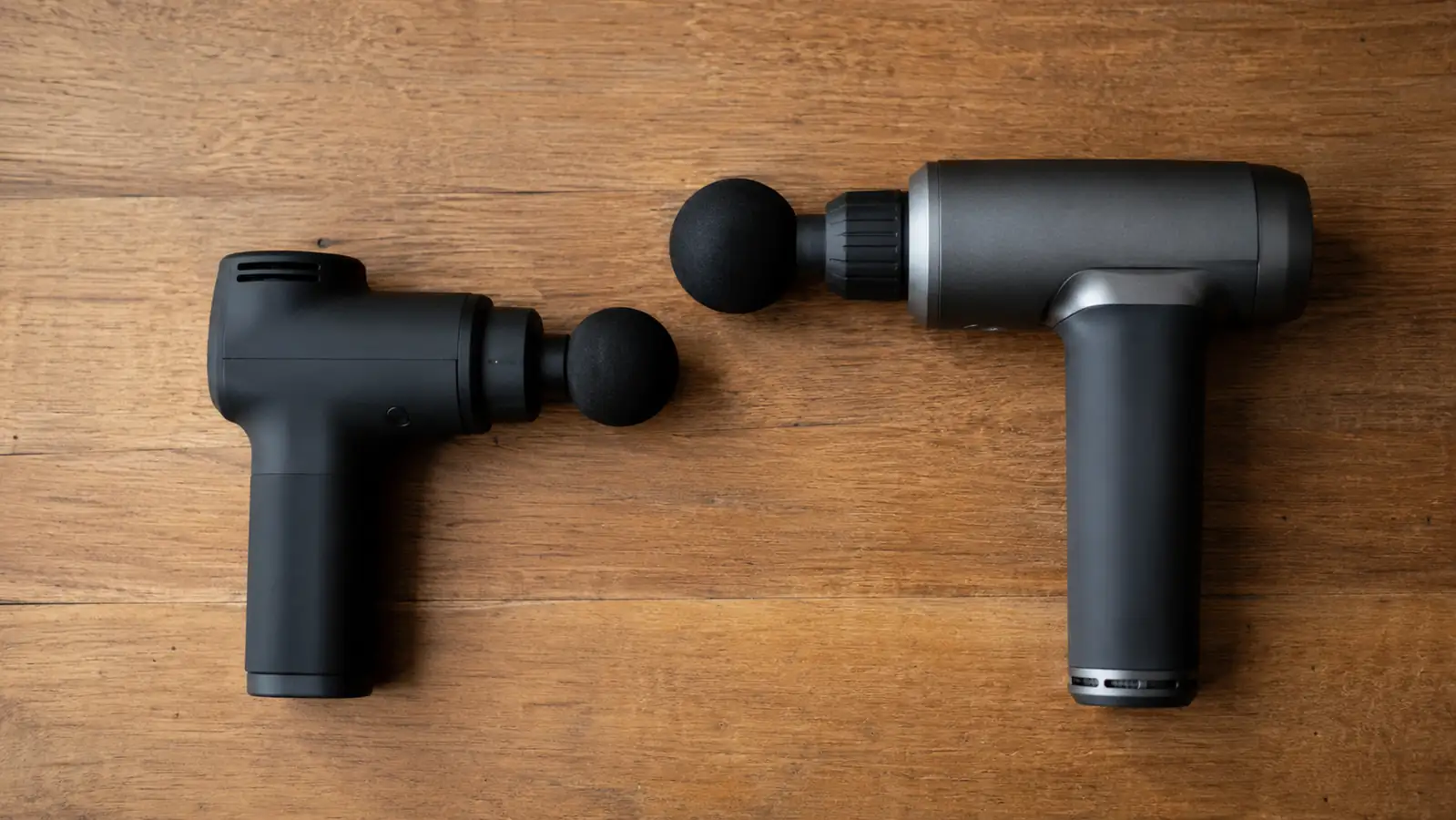 Two massage guns side by side on a table, a budget model and a premium model, for a size and build comparison