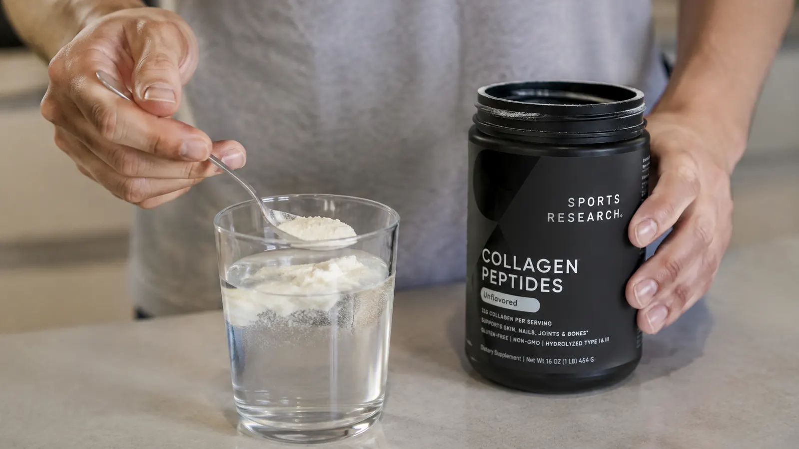 Hand stirring clumped collagen powder floating on top of a glass of cold water